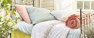 Tagesbett mit geblümten und gestreiften Kissen, umgeben von Pflanzen auf einer sonnigen Terrasse.