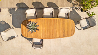 Draufsicht auf einen stabilen 4Seasons Tisch Capri 240 x 110 cm Teakholztisch mit sechs gepolsterten Stühlen und einem Pflanzenaufsatz auf einer mit Steinfliesen ausgelegten Terrasse.