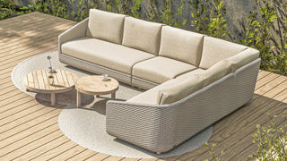 Das 4Seasons Lounge-Set Casanova Rope Latte von Zeo Living, ein L-förmiges beiges Outdoor-Lounge-Set mit wetterfesten Kissen und einem Seil-Muster-Design, steht auf einer Terrasse mit zwei runden Holztischen und üppigem Grün im Hintergrund.