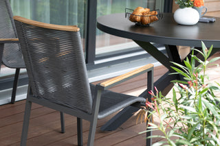 Auf der Terrasse steht ein DeVries-Esstisch Livingston Ø120cm mit einem Korbstuhl, geschmückt mit einem Drahtkorb voller Croissants und umgeben von üppigen grünen Pflanzen.