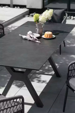 Der DeVries Ausziehtisch Hammond 200/260x90cm in Dunkelgrau mit Aluminium-Gestell bietet eleganten Platz für Tassen, einen Napfkuchen auf einem Teller und eine Vase mit Blumen.