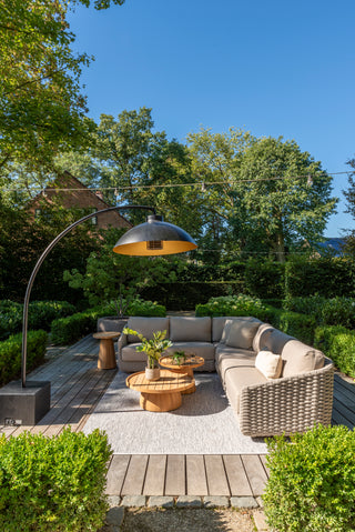 Der Sitzbereich im Freien verfügt über ein Zeo Living 4Seasons Lounge-Set Casanova Rope Latte mit einer geschwungenen Lampe, einem Sofagarnitur, Holztischen und üppigem Grün unter einem klaren blauen Himmel. Entspannen Sie bequem und stilvoll mit diesem einladenden Lounge-Set, das jeden Raum ergänzt.