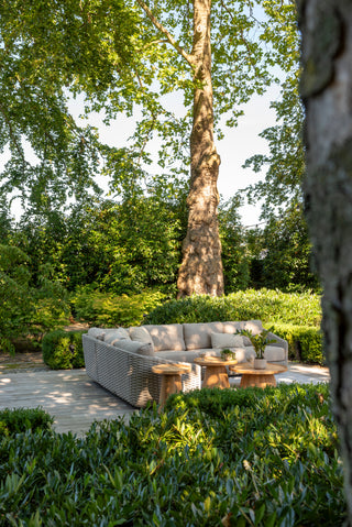 Sitzbereich im Freien mit dem Zeo Living 4Seasons Lounge-Set Casanova Rope Latte im Seilmuster-Design, begleitet von runden Holztischen. Üppige grüne Bäume und Büsche umgeben den Raum, während wetterfeste Kissen für Komfort bei jedem Wetter sorgen.