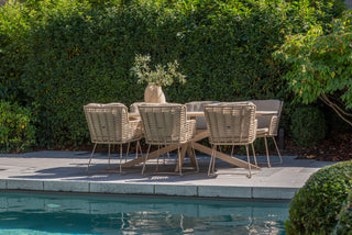 Ein Rope-Geflecht-Tisch und 4Seasons Dining-Stuhl Fabrice Latte Korbstühle bilden ein elegantes Outdoor-Esszimmerset am Pool. Eine Vase mit Grünpflanzen verstärkt die Atmosphäre, umgeben von üppigem Laub für das perfekte Outdoor-Erlebnis.