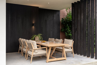Zeitgenössischer Essbereich im Freien mit Holztisch und 4Seasons Dining-Stuhl Julia Teakholzstühlen mit Kissen vor dunklen Holzwänden. Eine üppige Pflanze verstärkt den natürlichen Charme der Umgebung, während die Teakholzoberfläche für Langlebigkeit dieser eleganten und wetterfesten Einrichtung sorgt.