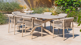 Das 4Seasons Tisch Prado Keramik/Edelstahl 240 x 105 cm Latte-Set besteht aus sechs Korbstühlen und einer weißen Schüssel auf einer gefliesten Terrasse, umgeben von üppigem Grün.